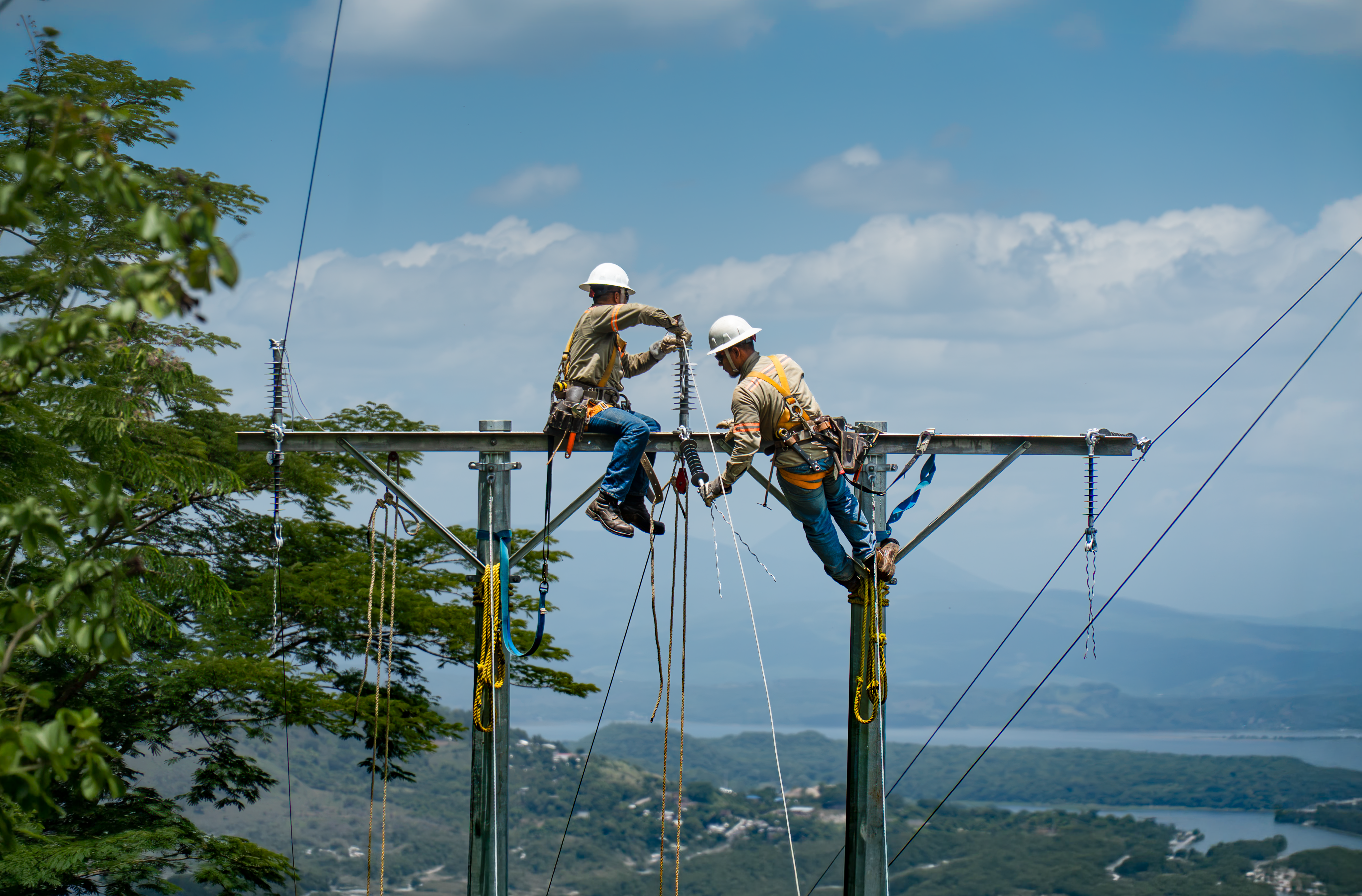 Dos trabajadores con equipo de seguridad instalando componentes de alta tensión en una torre de metal al aire libre