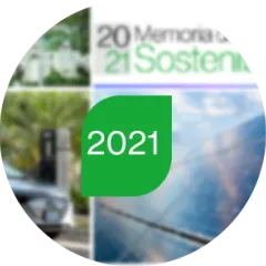 A group of people wearing white shirts and green caps stand outdoors surrounded by trees and greenery. Many have one arm raised, suggesting a group gesture or celebration.