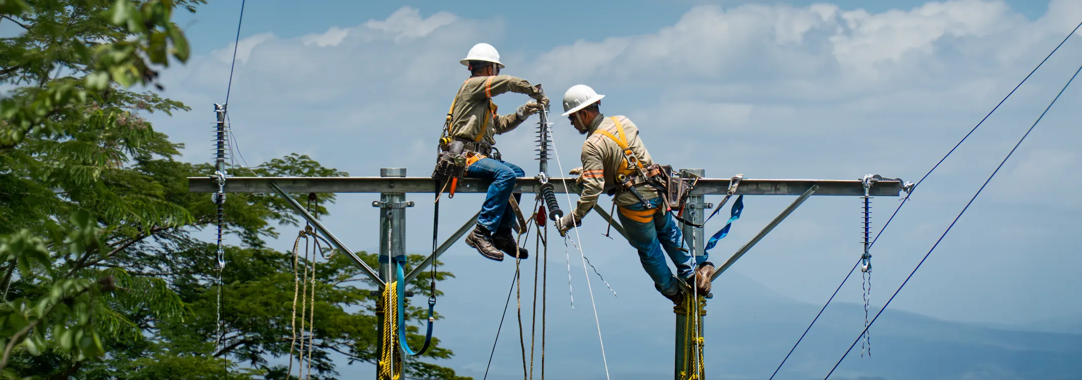 Dos trabajadores con equipo de seguridad instalando componentes de alta tensión en una torre de metal al aire libre