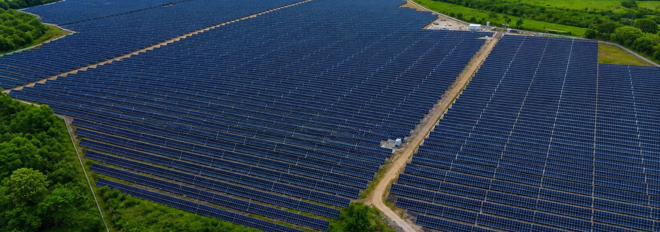 Vista aérea de un extenso parque solar con miles de paneles fotovoltaicos azules instalados en un entorno rural verde. La planta está rodeada de frondosa vegetación, un río serpenteante y colinas al fondo bajo un cielo claro