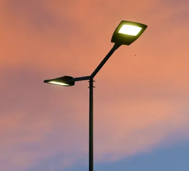 A group of people wearing white shirts and green caps stand outdoors surrounded by trees and greenery. Many have one arm raised, suggesting a group gesture or celebration.