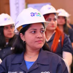 A group of women wearing white hard hats with the "aes" logo and dark blue uniforms. The individuals' faces are blurred for privacy.